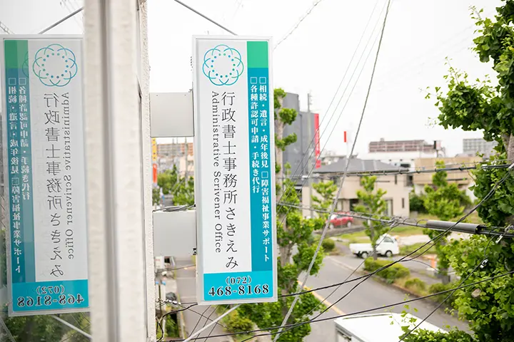 事務所の窓から「行政書士事務所さきえみ」の看板を望む